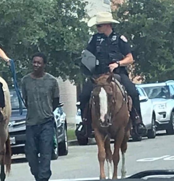 Black Man pulled by police officer on horse with a leash