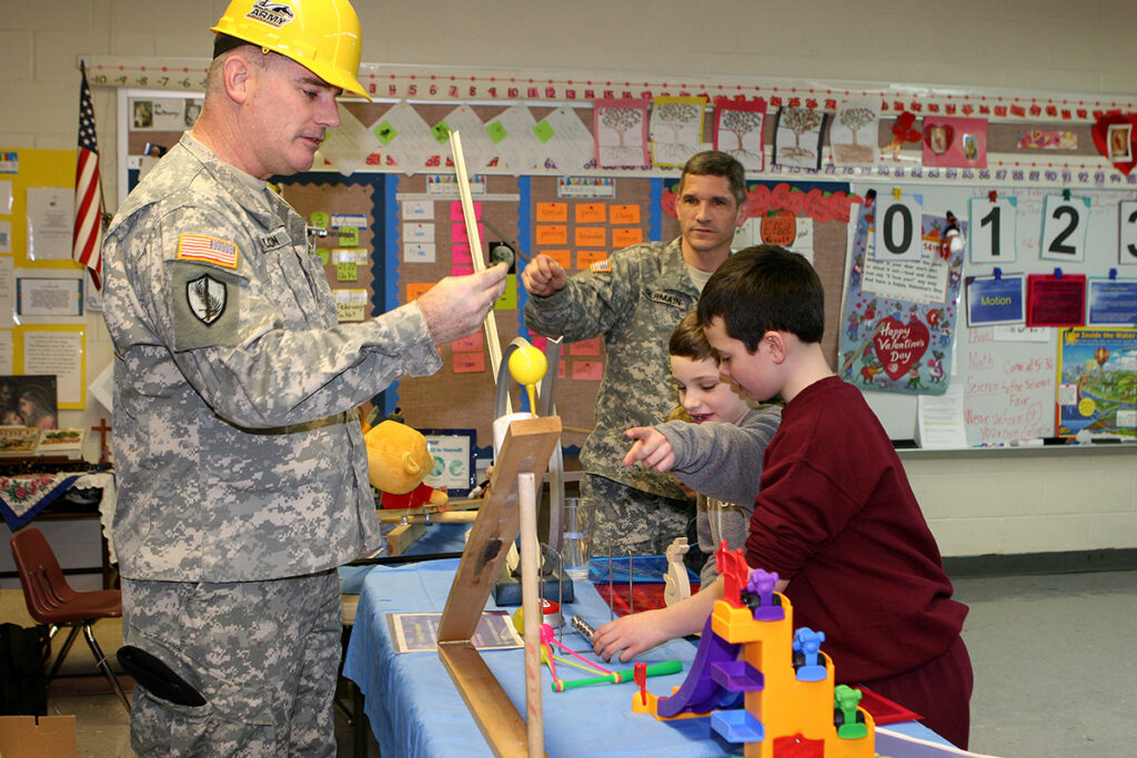 Col. Raymond Nelson, Academy Professor and Physics department head talks to (l to r) John O'Donnell, Christopher Germain and Col. Jesse Germain, DPE Academy Professor on kinetic energy at the Sacred Heart of Jesus school in Highland Falls annual Science Fair. Academy science, math and physics professors attend the fair to give demonstrations to children to show how fun science is and how physics and science are applied to everyday life.